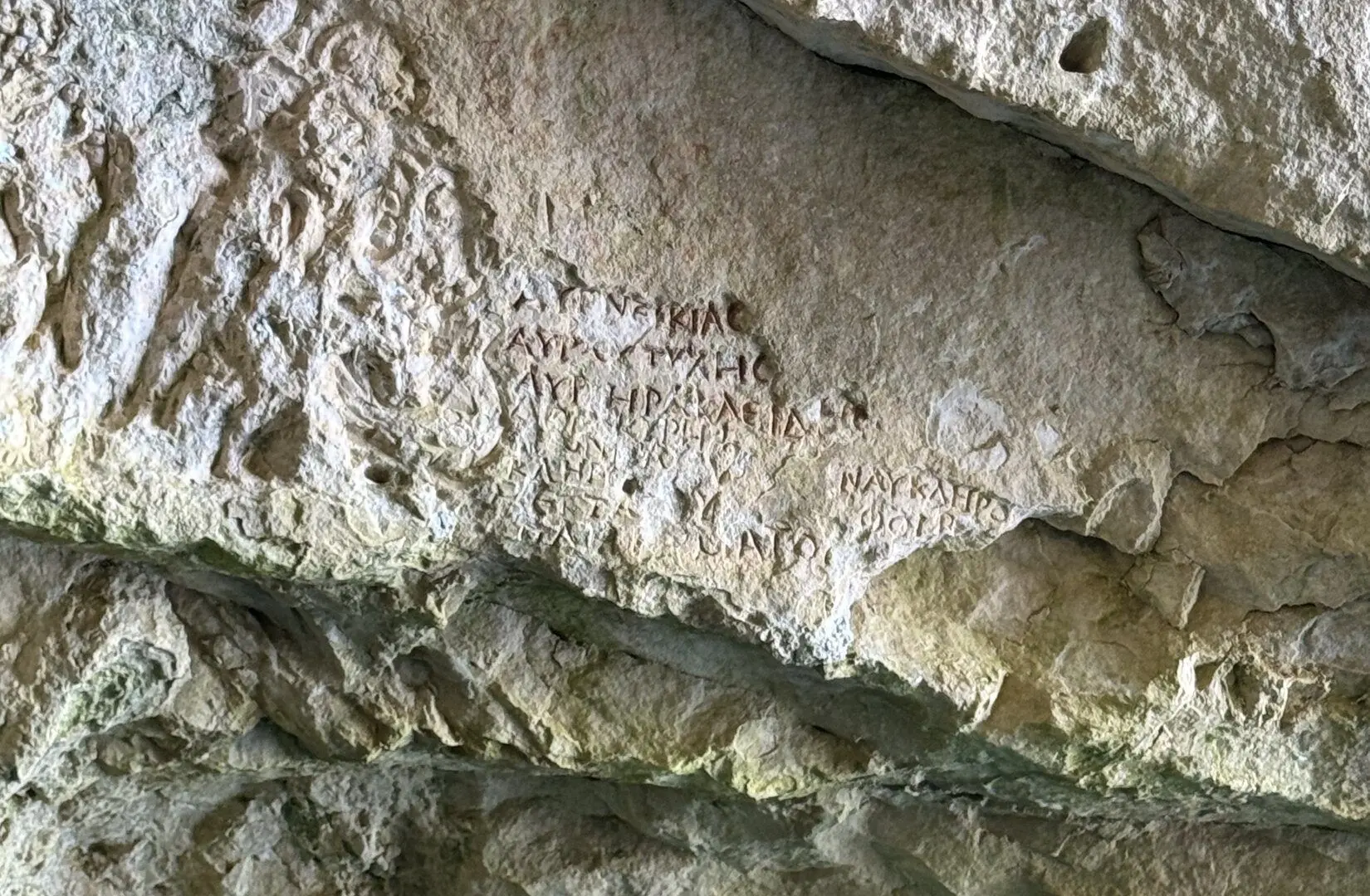 Greek letters carved into a pale limestone rock face at Shpella e Priftit, the Priest's Cave